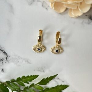 Gold evil eye earrings on marble background
